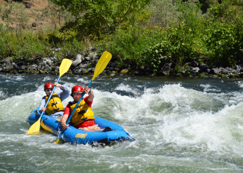 Two trip participants in a blue raft smiling as they navigate a river's whitewater rapids