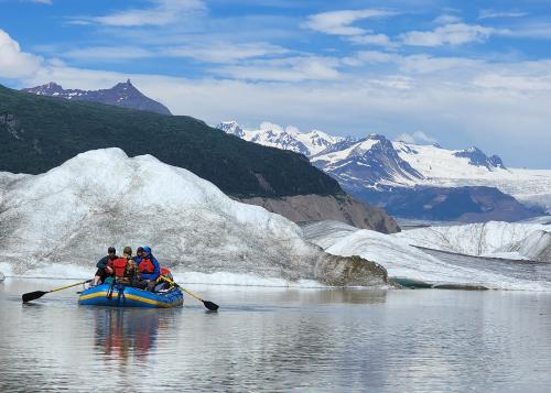 Trip participants on a raft in front of icebergs with snow-capped mountain peaks in the background