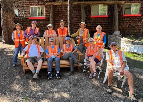 A group of 11 smiling participants sitting and standing and all wearing orange worker's vests