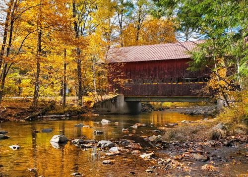 Iconic Vermont covered bridge over a river, surrounded by colorful autumn foliage