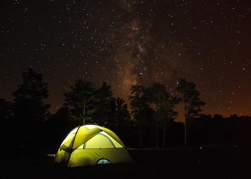 A glowing light green camping tent at night time with stars in the sky