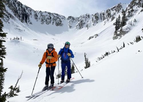 Two skiers smile and pose at the bottom of a snowy basin.
