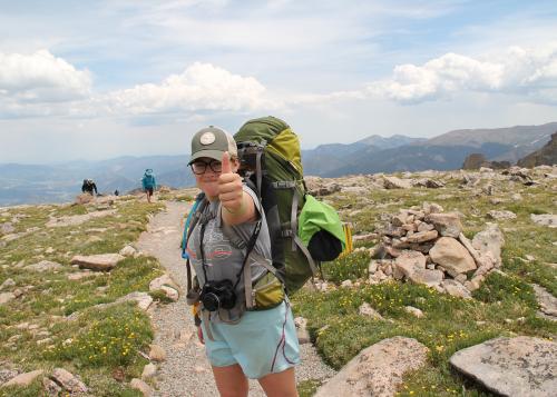 Teen girl facing camera and giving a thumbs up while backpacking in the Rocky Mountains
